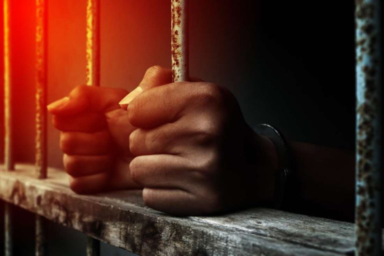 Close up prisoner holding bar in jail. Fotosearch