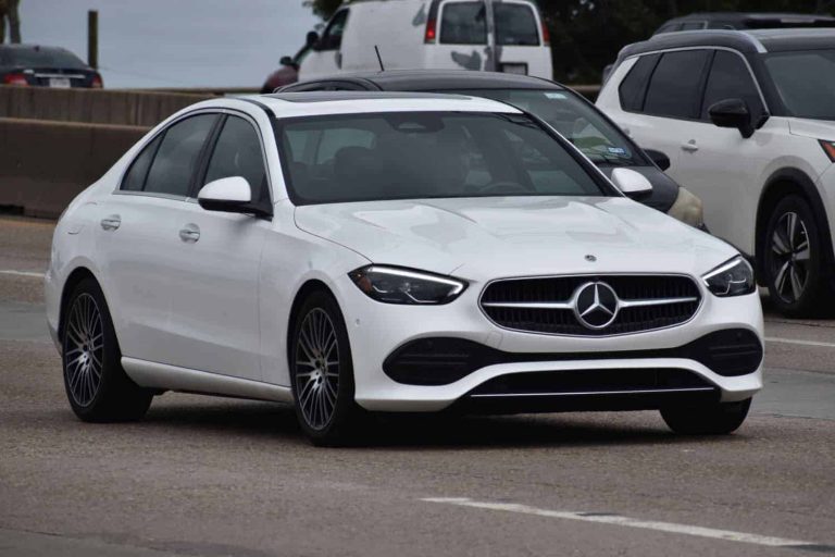 A portrait of a white luxury Mercedes-Benz C-Class sedan traveling down a highway in moderate traffic