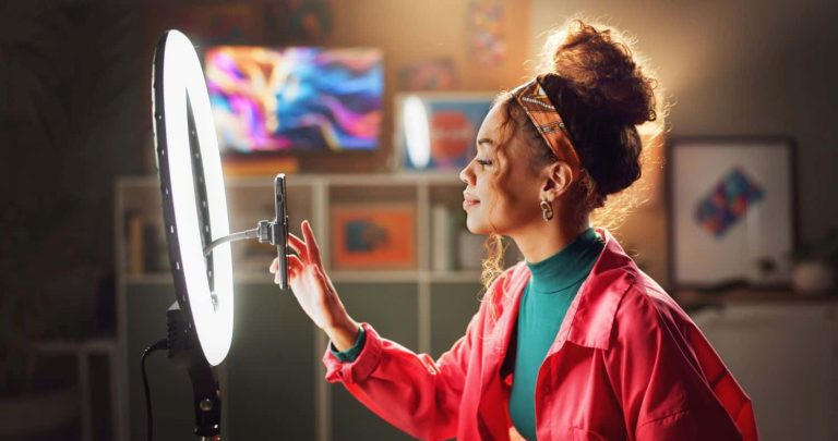 Woman, influencer and phone with ring light for video recording, vlogging or online tutorial at home. Young, female person or vlogger setting up mobile smartphone for advice, tips or content creation