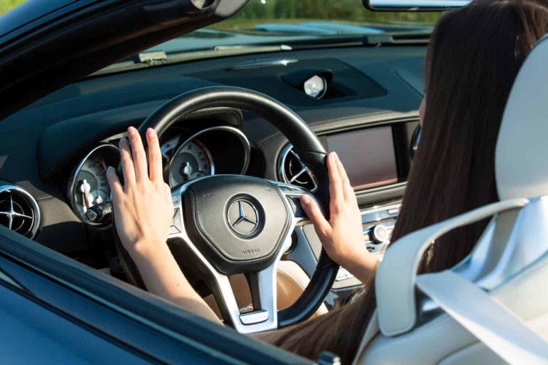 Closeup on female hands driving Mercedes Benz car luxury transportation lifestyle. Mercedes Benz SL550 convertible on the road.