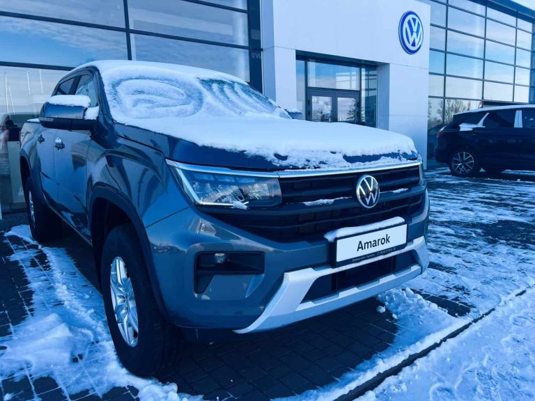 Snow-covered Volkswagen Amarok pickup truck parked outside a dealership on a winter day