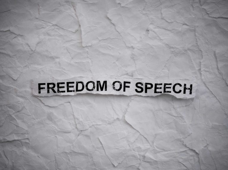 Crumpled piece of a paper with words Freedom of Speech on torn white paper pieces background.