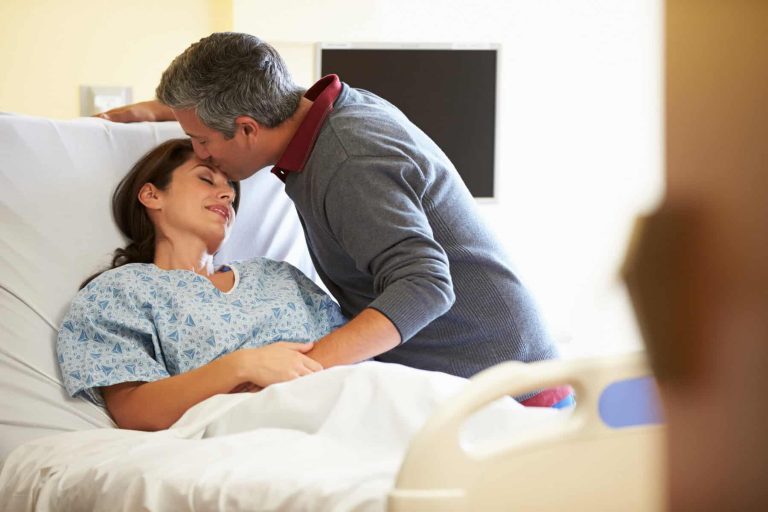A husband kissing his wife's forehead in a hospital bed