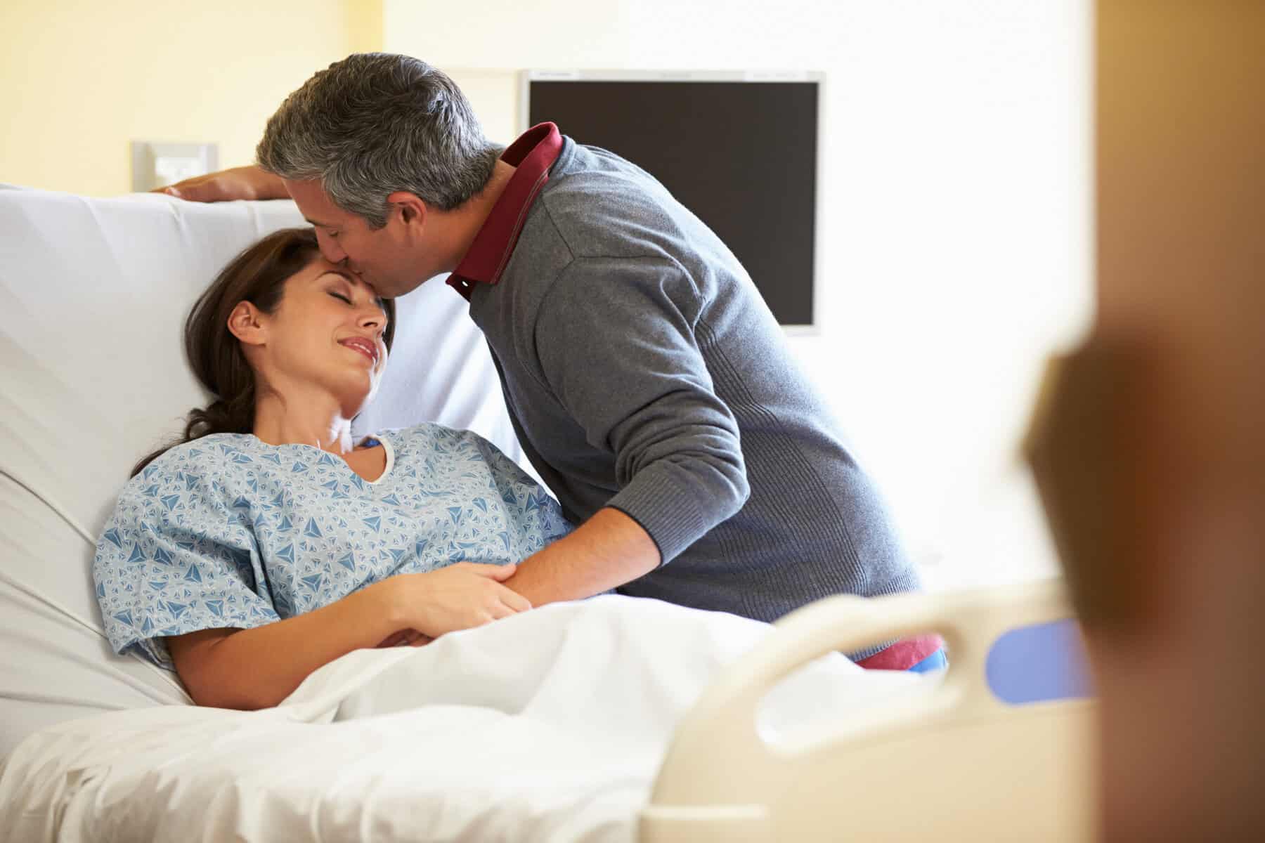A husband kissing his wife's forehead in a hospital bed