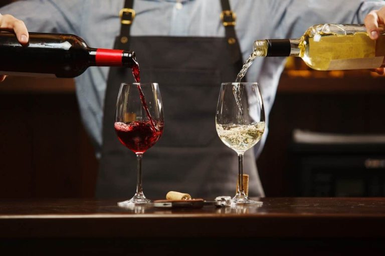 Male sommelier pouring red and white wine into long-stemmed wineglasses