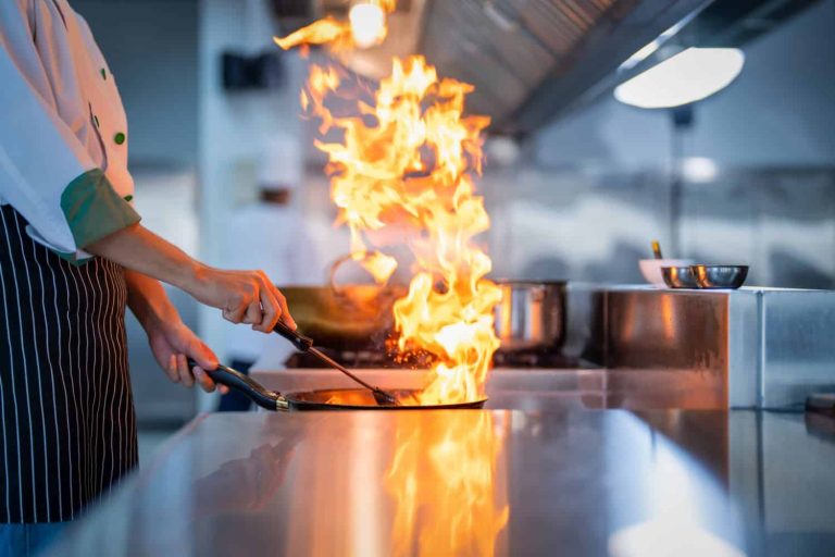 Chef in restaurant kitchen at stove and pan cooking flambe on food