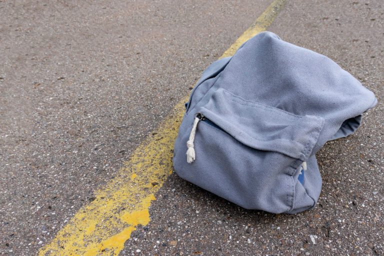 Lonely grey casual style backpack standing on asphalt road with yellow line road marking with copy space