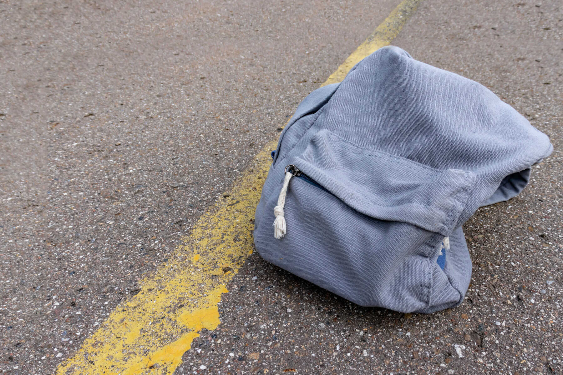 Lonely grey casual style backpack standing on asphalt road with yellow line road marking with copy space