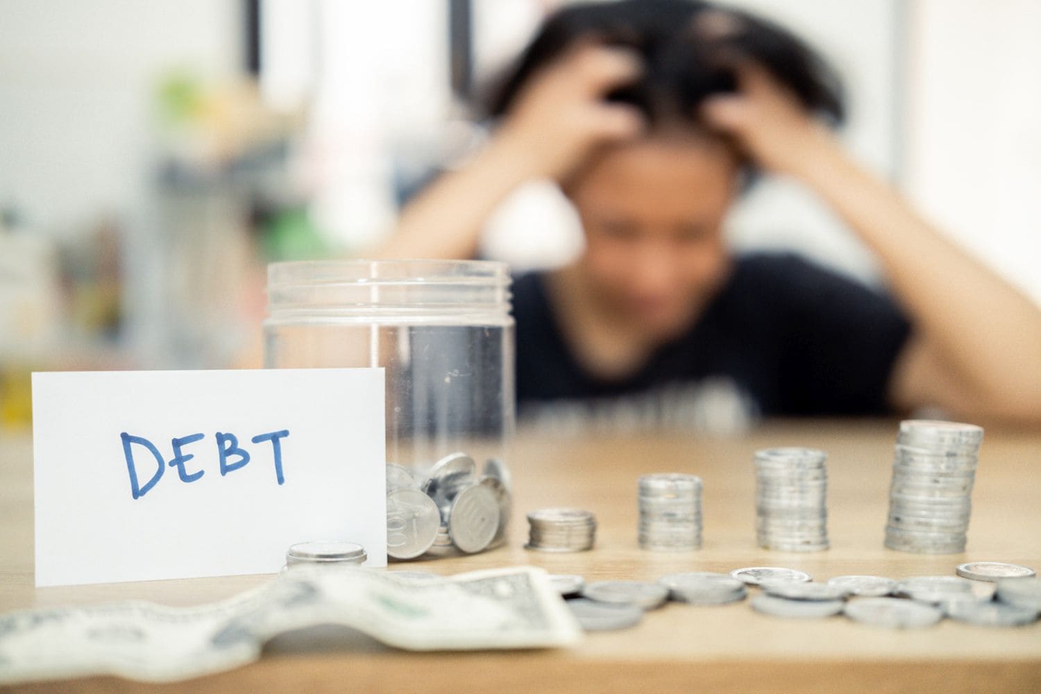 A woman sits at a table, looking distressed, with piled coins and a debt note. This scene expresses the concept of financial burden, economic challenges, and personal reflections on money management.