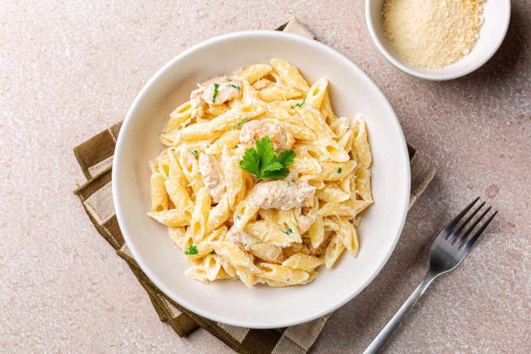 Chicken Alfredo penne, creamy pasta wich parmesan cheese in a white plate. Directly above.