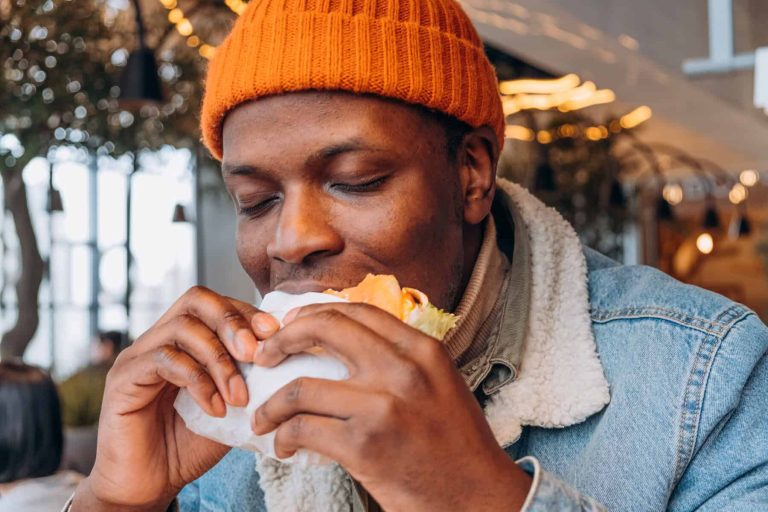 African American Man in Orange Beanie Savoring the First Bite of a Juicy Burger