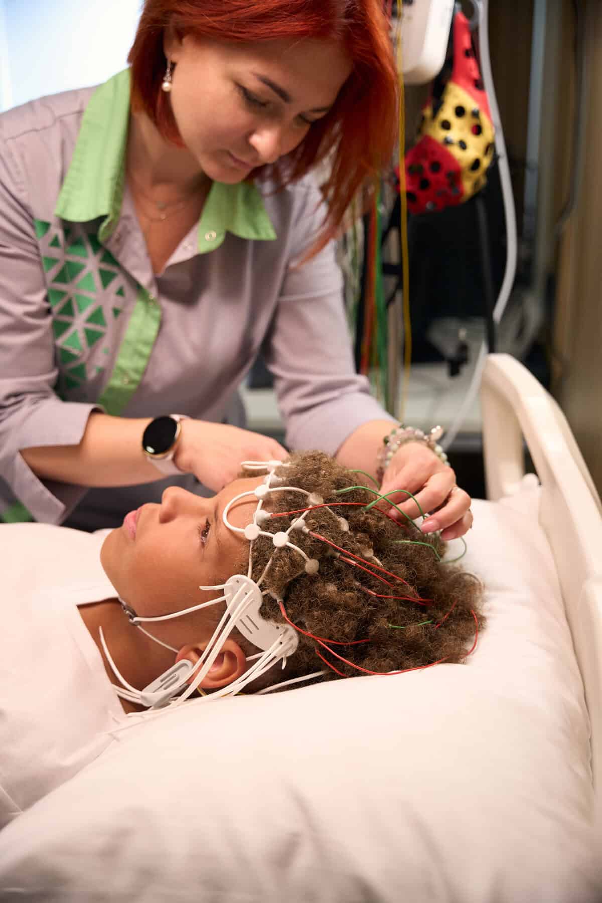 Woman leans over the patient to fine-tune the EEG setup