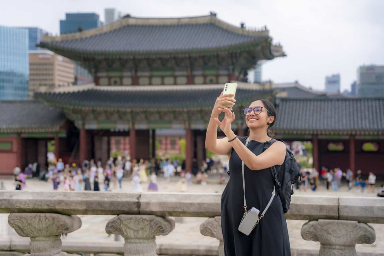 Young happy Latina woman in a black dress admiring the traditional architecture and taking selfie at Gyeongbokgung Palace, South Korea.