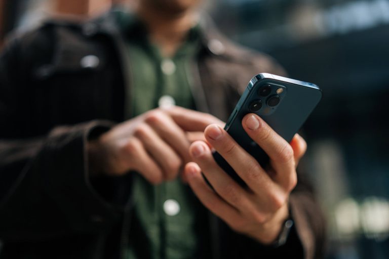 Close-up hands of unrecognizable man holding and using smartphone standing on city street, browsing internet, checking social media, using mobile application.