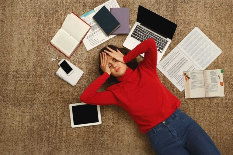 Tired student girl lying on the floor with books and gadgets