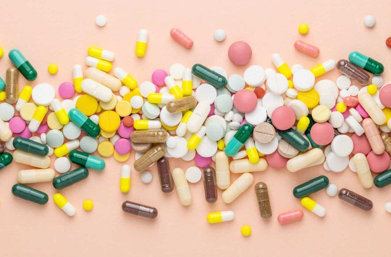 Many different pills on pink background. Prescription pills and vitamins. Flat lay and space for text.