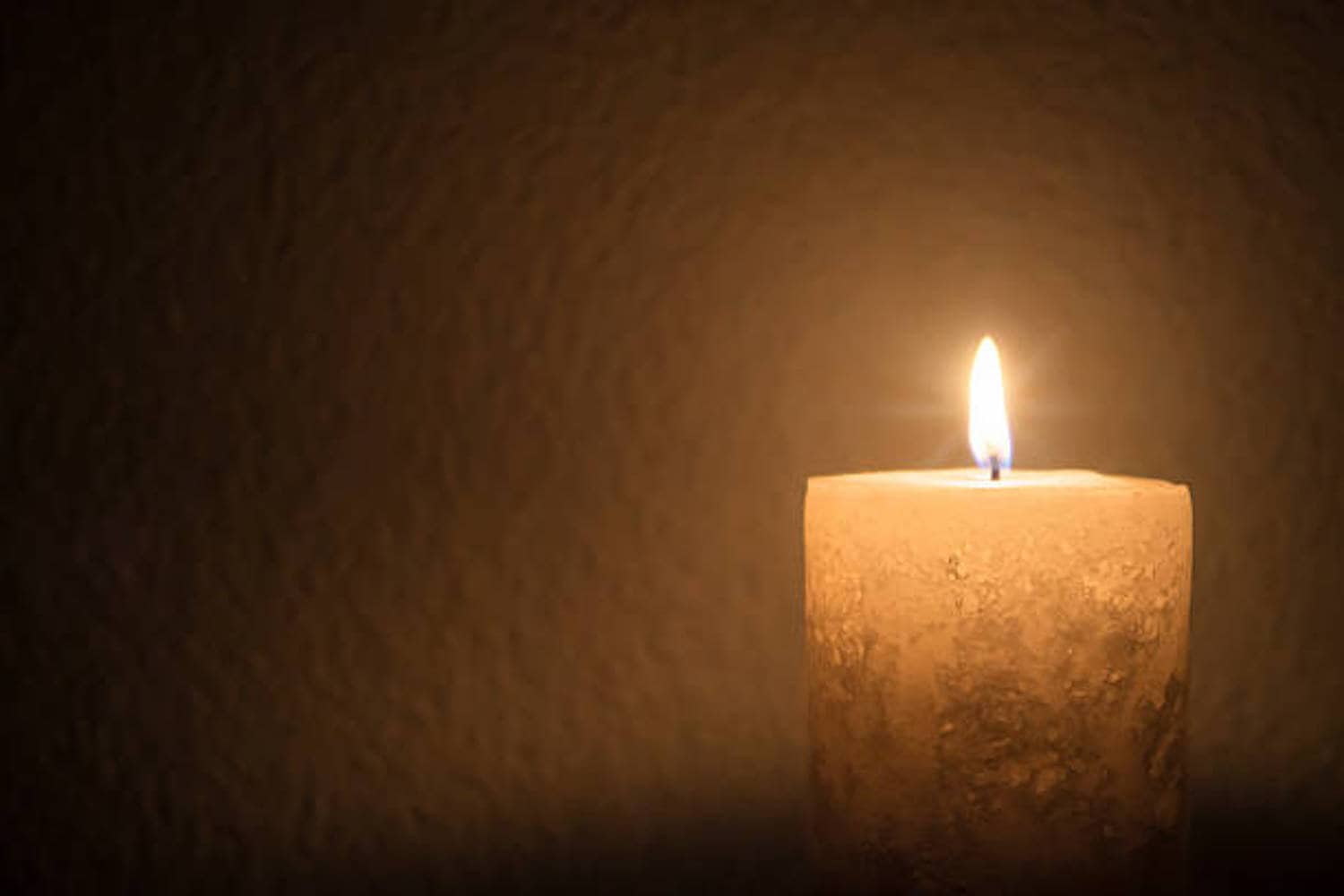 Single thick candle burns brightly in dark room - landscape interior