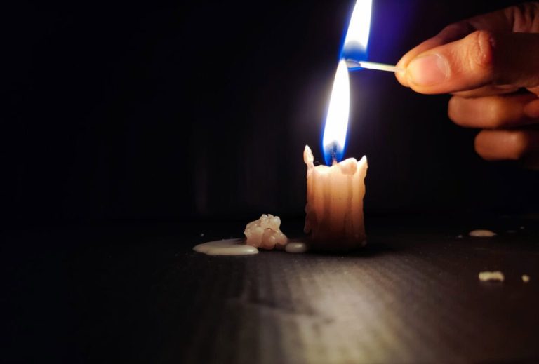 Stock photo of a human hand holding lighted matchsticks with yellow and blue color flame for lighting up the white color small candle on black dark background. focus on object.