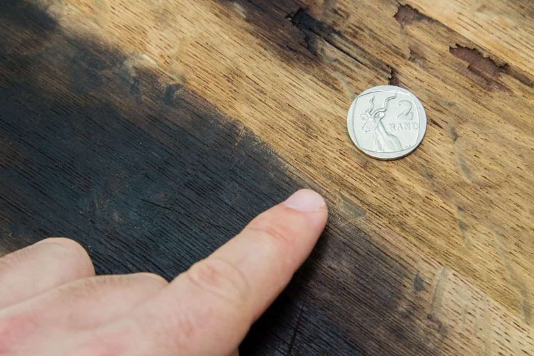 A Caucasian finger pointing towards a South African two rand coin on a wooden background.