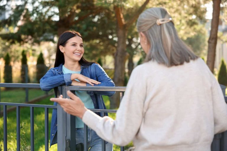 Friendly relationship with neighbours. Happy women talking near fence outdoors
