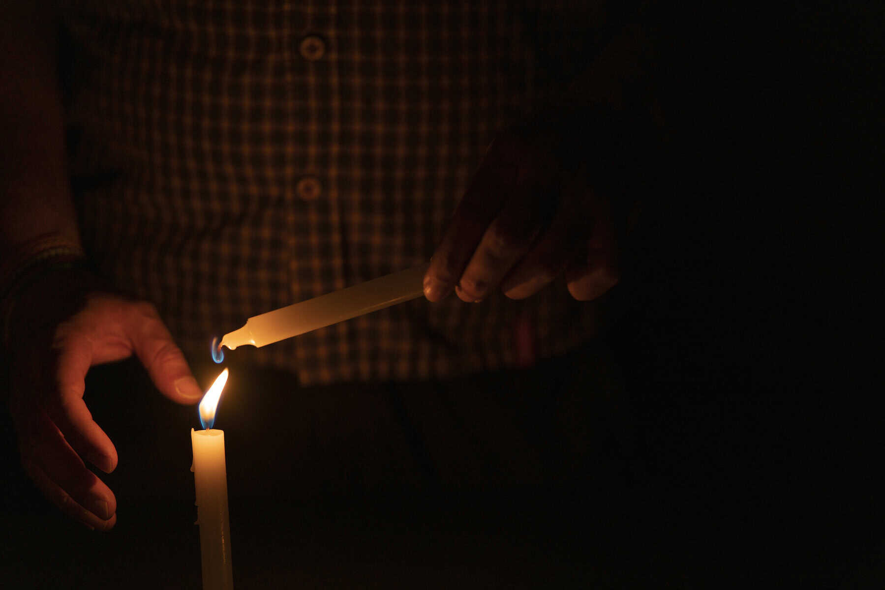 Close up of man's hand lighting a candle in the dark