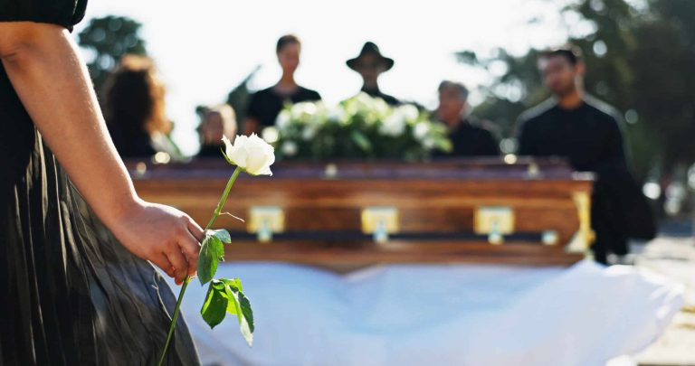 Hand, rose and woman at graveyard for funeral ceremony, grief and memorial service outdoor with family. Flower, death and person by coffin at cemetery for mourning, peace and respect with back view