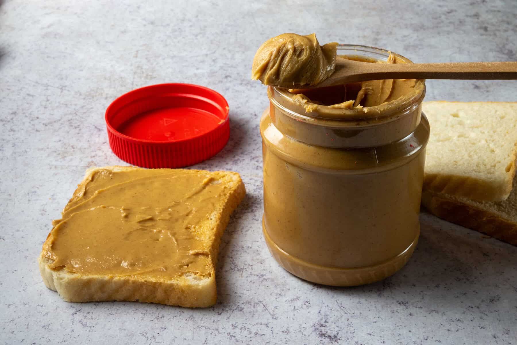 Peanut butter jar with bread and spoon on table