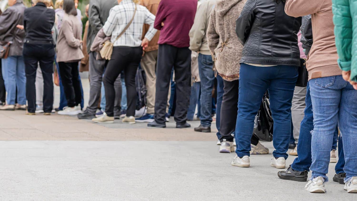 Group of anonymous diverse people standing in queue outdoors, long line of men and women, rear view. Concept of waiting, patience, urban life