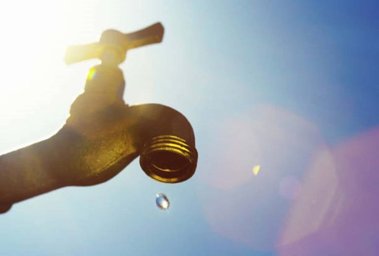 A single droplet falls from a faucet, symbolizing water scarcity or drought.