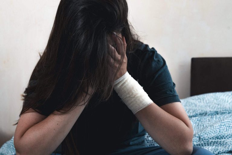 Young unhappy woman with a bandage on her hand hides her face. Depressed female scared and stressed suffering from depression and anxiety.
