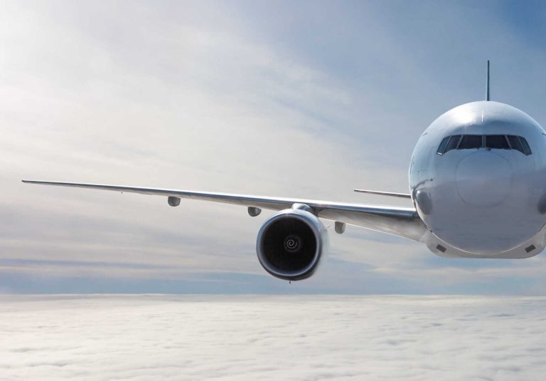 Front view of the white wide body passenger airplane flies in the air above the clouds