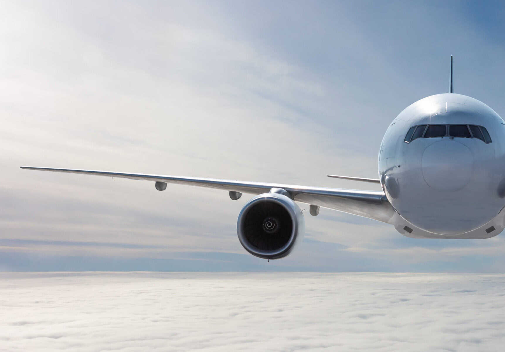 Front view of the white wide body passenger airplane flies in the air above the clouds
