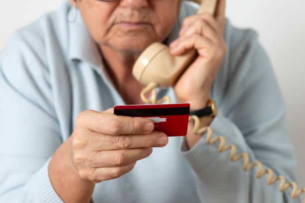 Senior woman using phone while holding credit card.