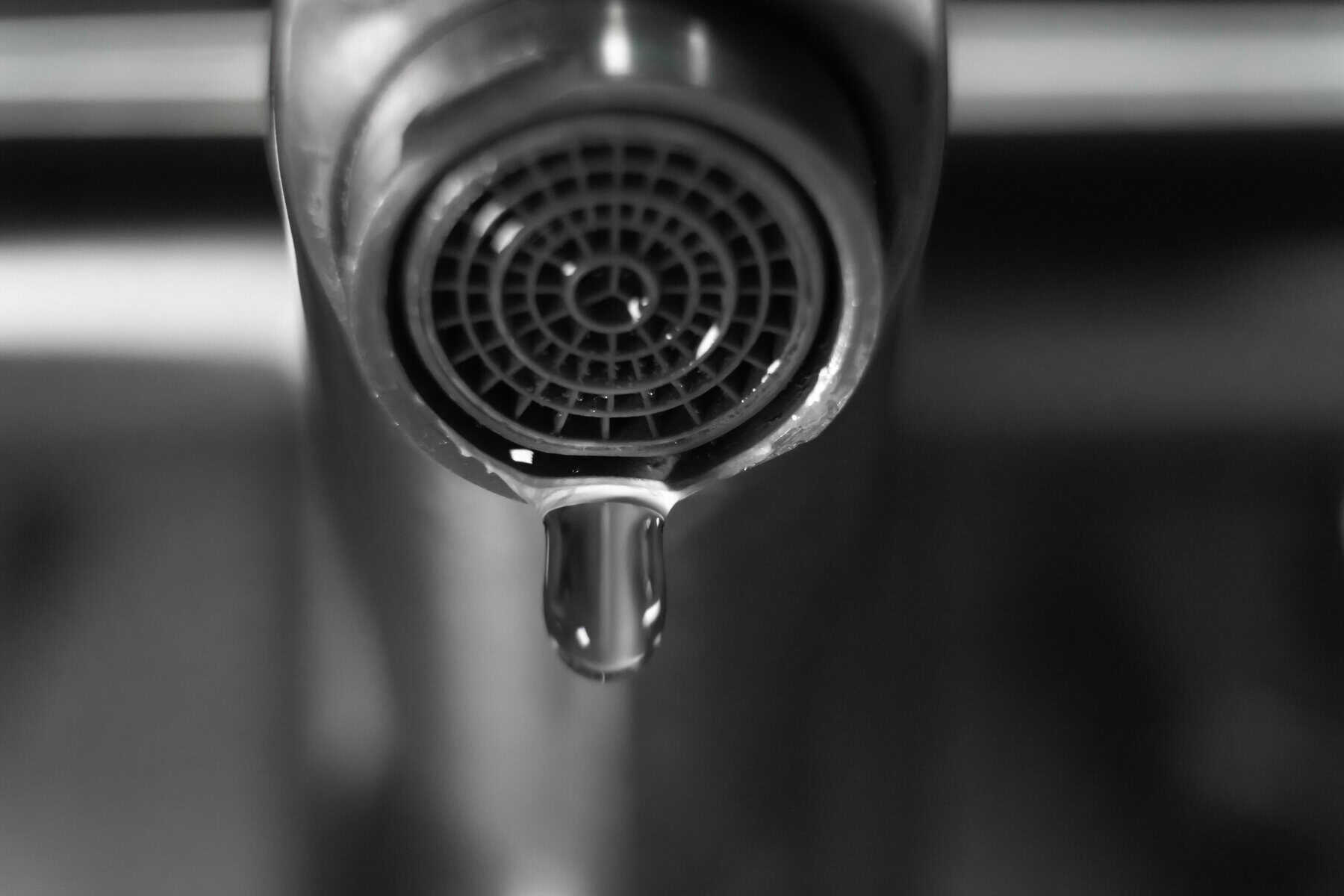 Close-up of a dripping faucet in monochrome, highlighting water waste, conservation, and plumbing problems, urging viewers to address leaks and promote responsible water usage