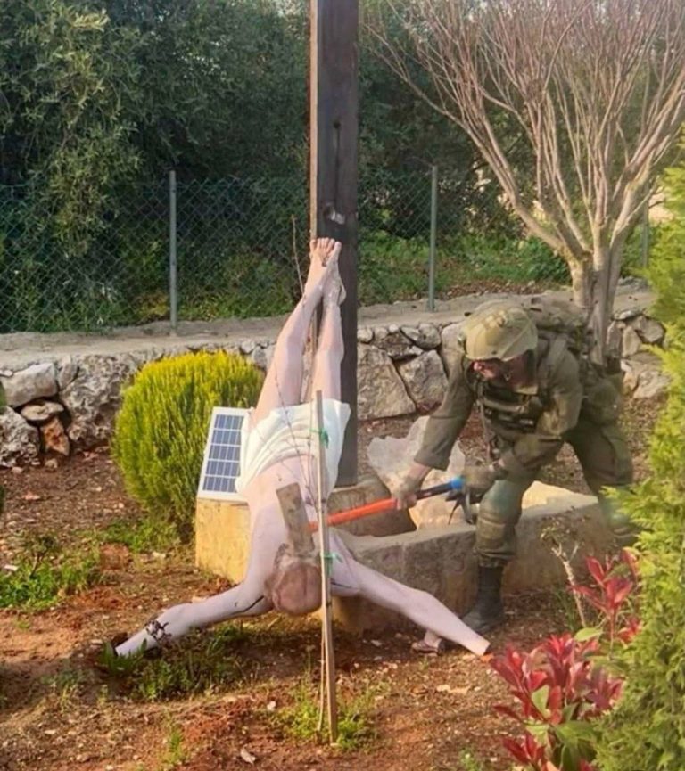 An Israeli soldier damages the head of a statue of Jesus, in Debel