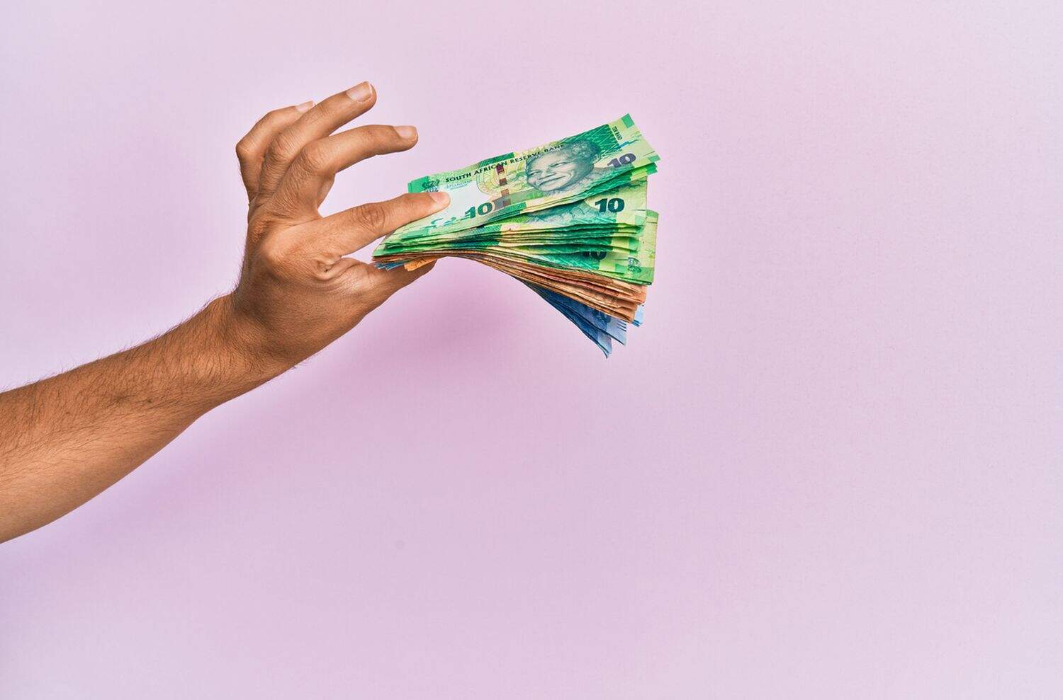 Hispanic hand holding south africa rands banknotes over isolated pink background.