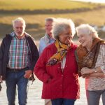 Group Of Smiling Senior Friends Walking Arm In Arm Along Shoreline Of Winter Beach