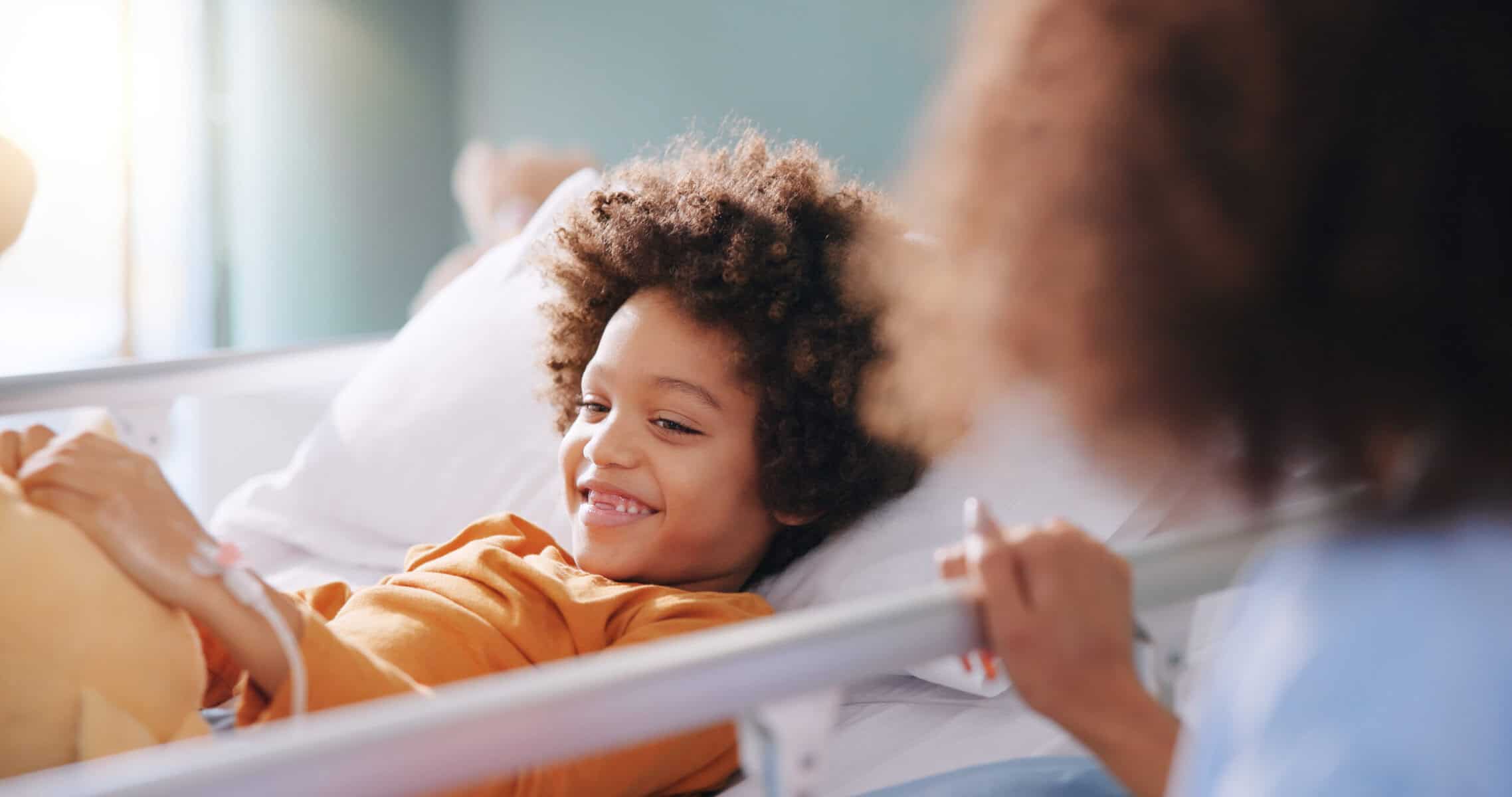 Kid, mother and smile in hospital bed with teddy bear for healthcare, medical support or surgery recovery. Mom, sick child and happy patient with toy for play, hand and healing illness with family