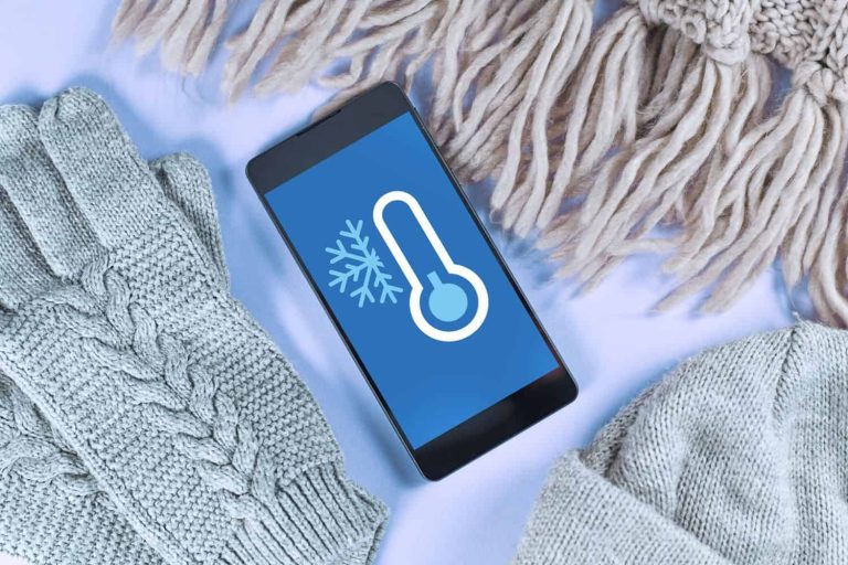Concept for cold temperatures with snow and minus degrees with mobile phone showing weather forecast surrounded by warm clothes