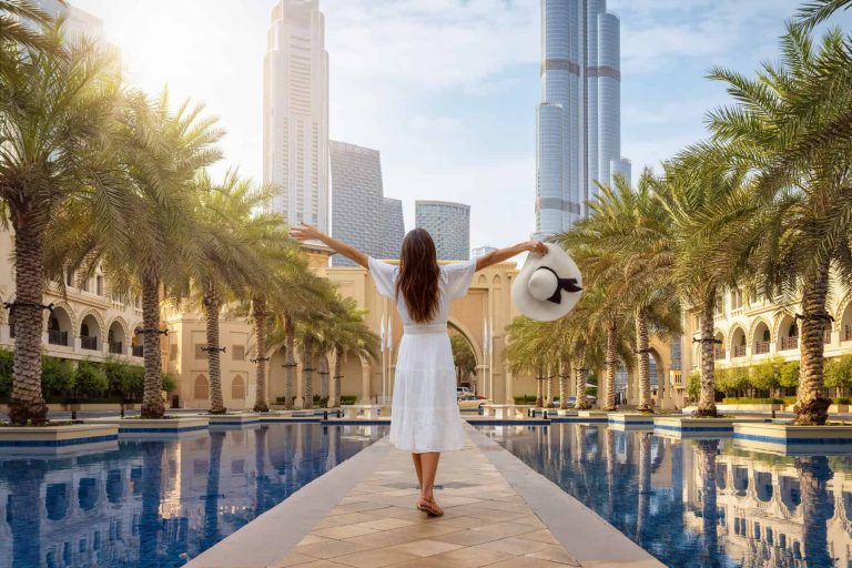 A tourist woman stands on a public square with palm trees at Downtown Dubai