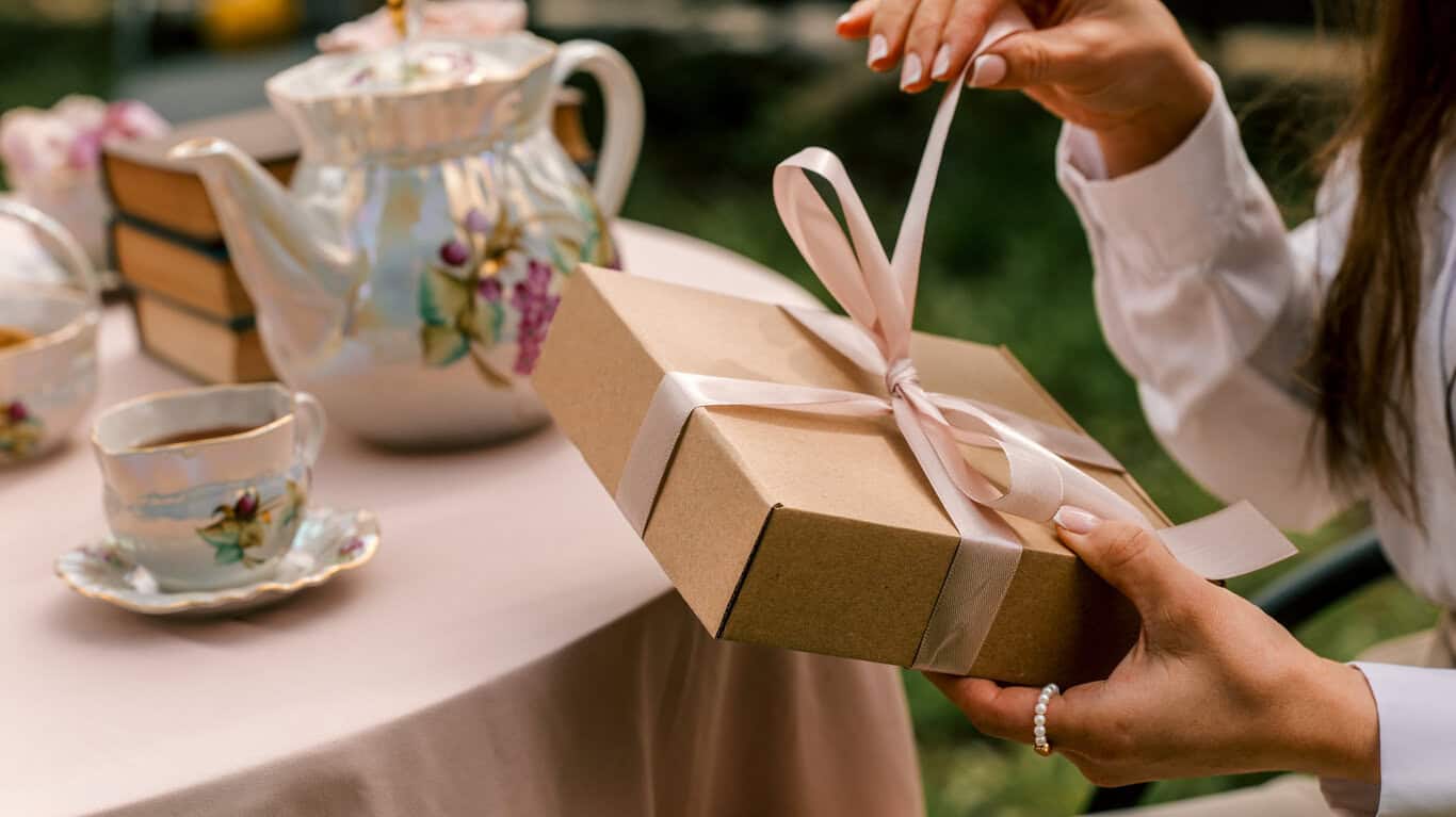 Woman opening a gift box tied with a pink ribbon at a tea party