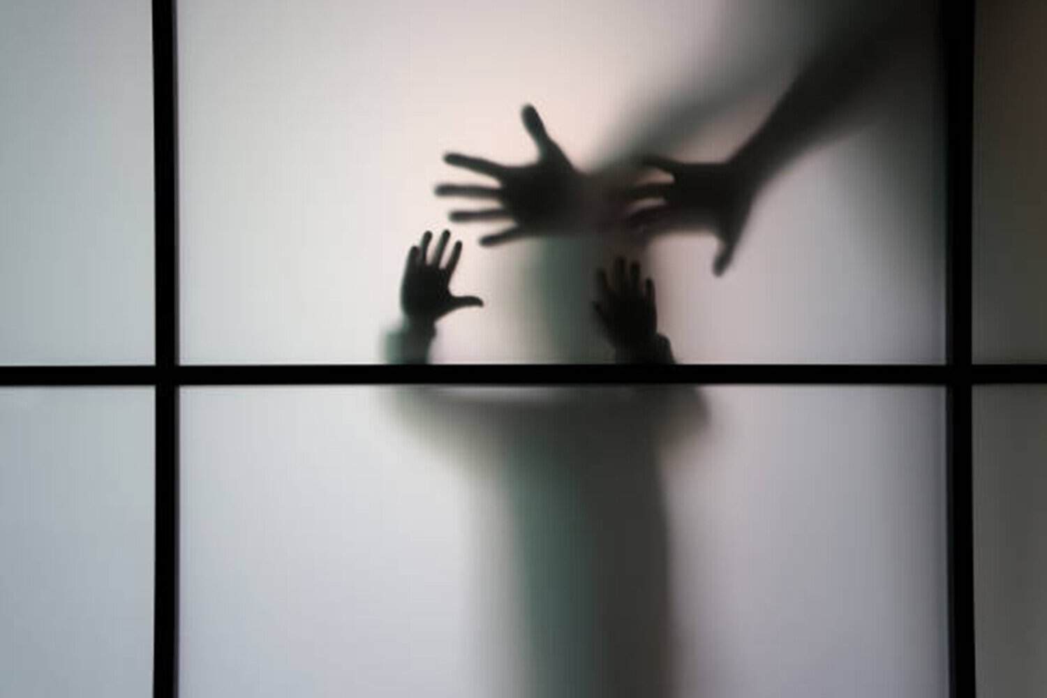 A woman stands behind of a frosted glass. She is afraid  of something.